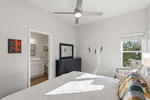 Ein Schlafzimmer mit einem Bett, einem Deckenventilator, einer Kommode, einem Nachttisch und einem Fenster mit Blick.