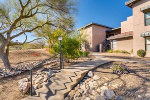 A building with a modern architectural style, a concrete pathway leading to the entrance, and a landscaped area with rocks and sparse vegetation. - Mountain, Canyon & Golf Course Views from all Windows in this corner 3 bedrm (Tucson)