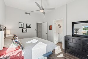 Ein Schlafzimmer mit einem Bett, einem Deckenventilator, einer Kommode und einer Tür zu einem anderen Raum.