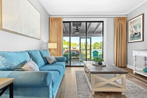 A living room with a sofa, coffee table, and a view through a glass door to an outdoor area. - 🦩Book Me Baby! See You at the Bayou in Miramar Beach🦩 (Miramar Beach)