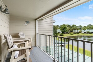 A balcony with a table and chairs, a railing, and a view of a pond and buildings. - 🦩Book Me Baby! See You at the Bayou in Miramar Beach🦩 (Miramar Beach)