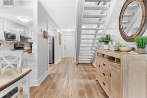 A modern kitchen with white cabinetry, a wooden dining table, and a staircase with a wooden railing. - 🦩Book Me Baby! See You at the Bayou in Miramar Beach🦩 (Miramar Beach)