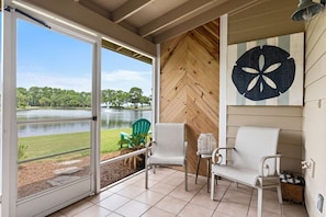 A room with a large sliding glass door leading to a lake view, two white chairs, a small table, and a wall-mounted artwork. - 🦩Book Me Baby! See You at the Bayou in Miramar Beach🦩 (Miramar Beach)