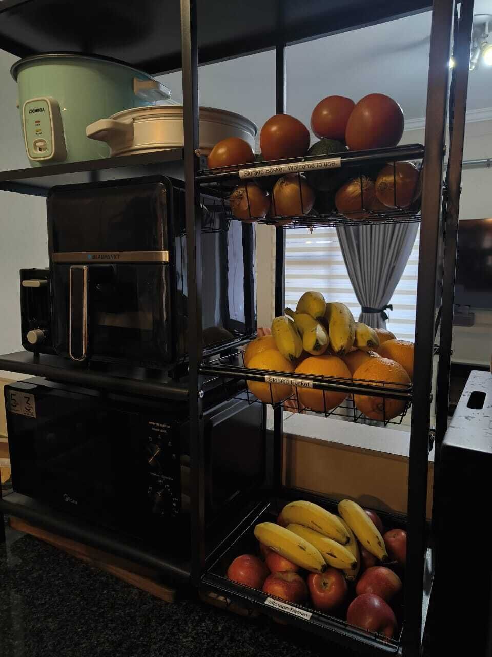 A kitchen with a coffee maker, a storage basket, and shelves with tomatoes, bananas, and oranges.