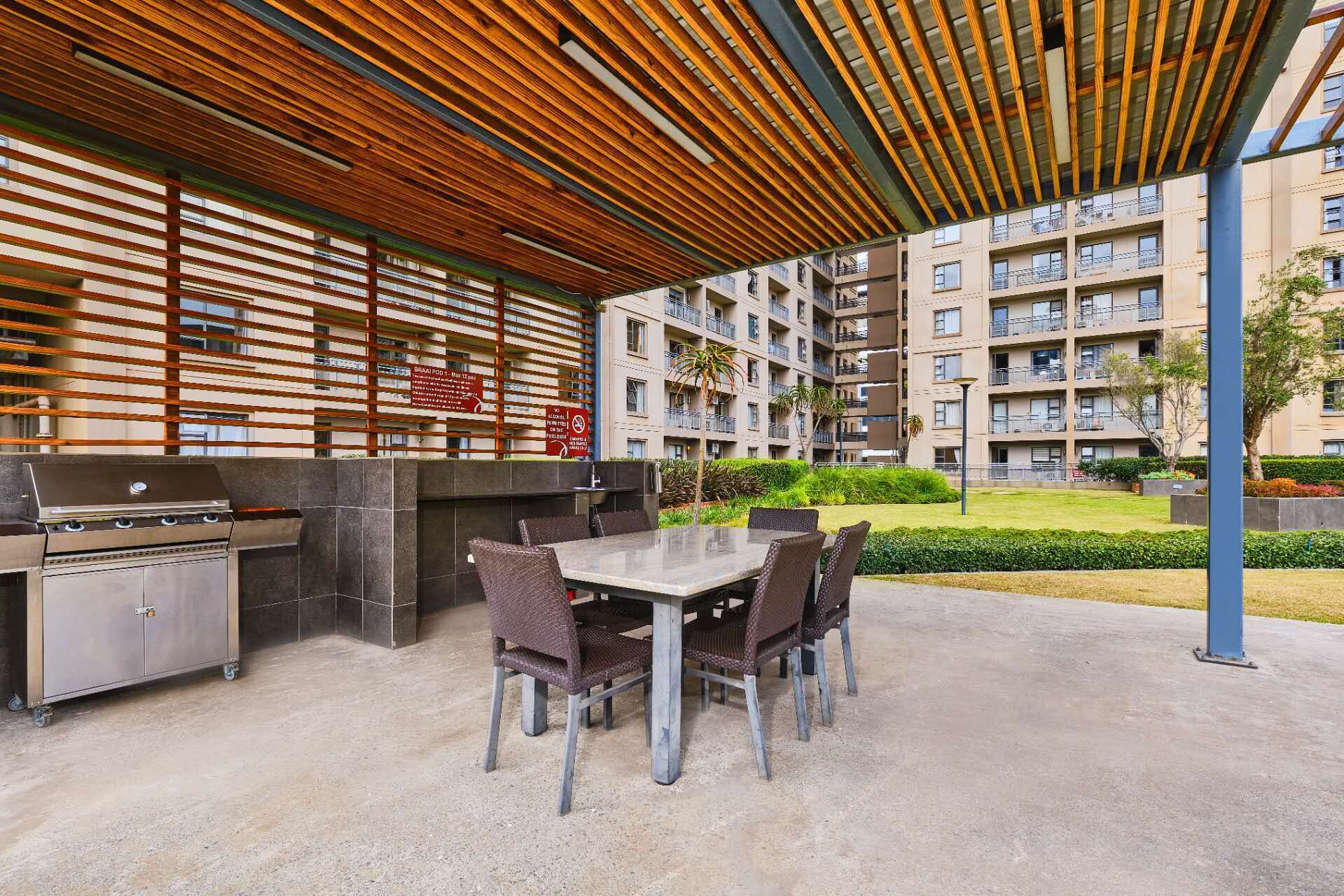 Un patio al aire libre con una parrilla y zona de estar, rodeado por un edificio con balcones.