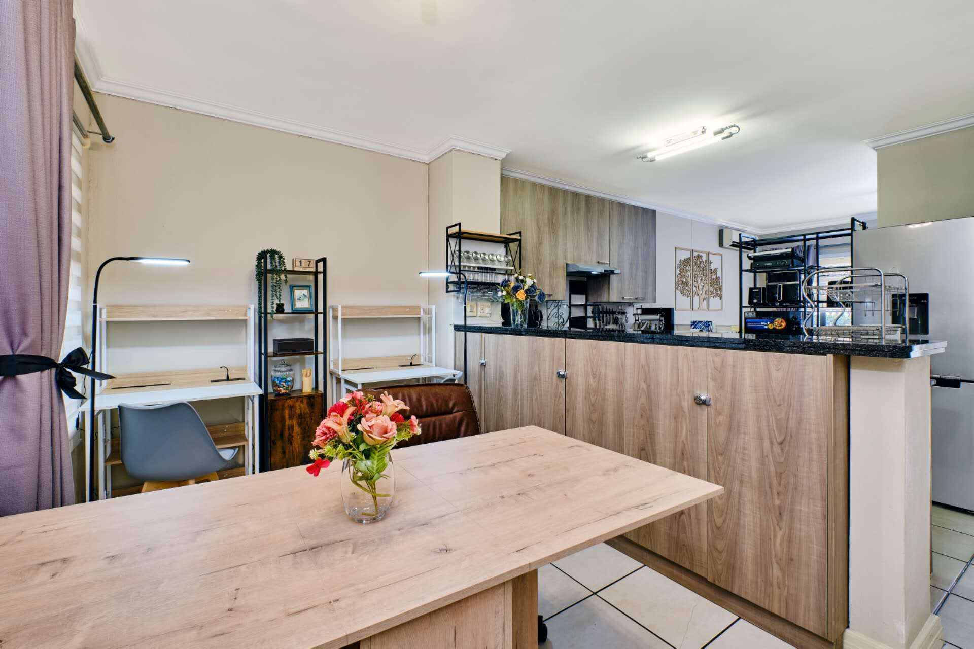 A modern kitchen with a wooden table, a vase of flowers, and a built-in oven.