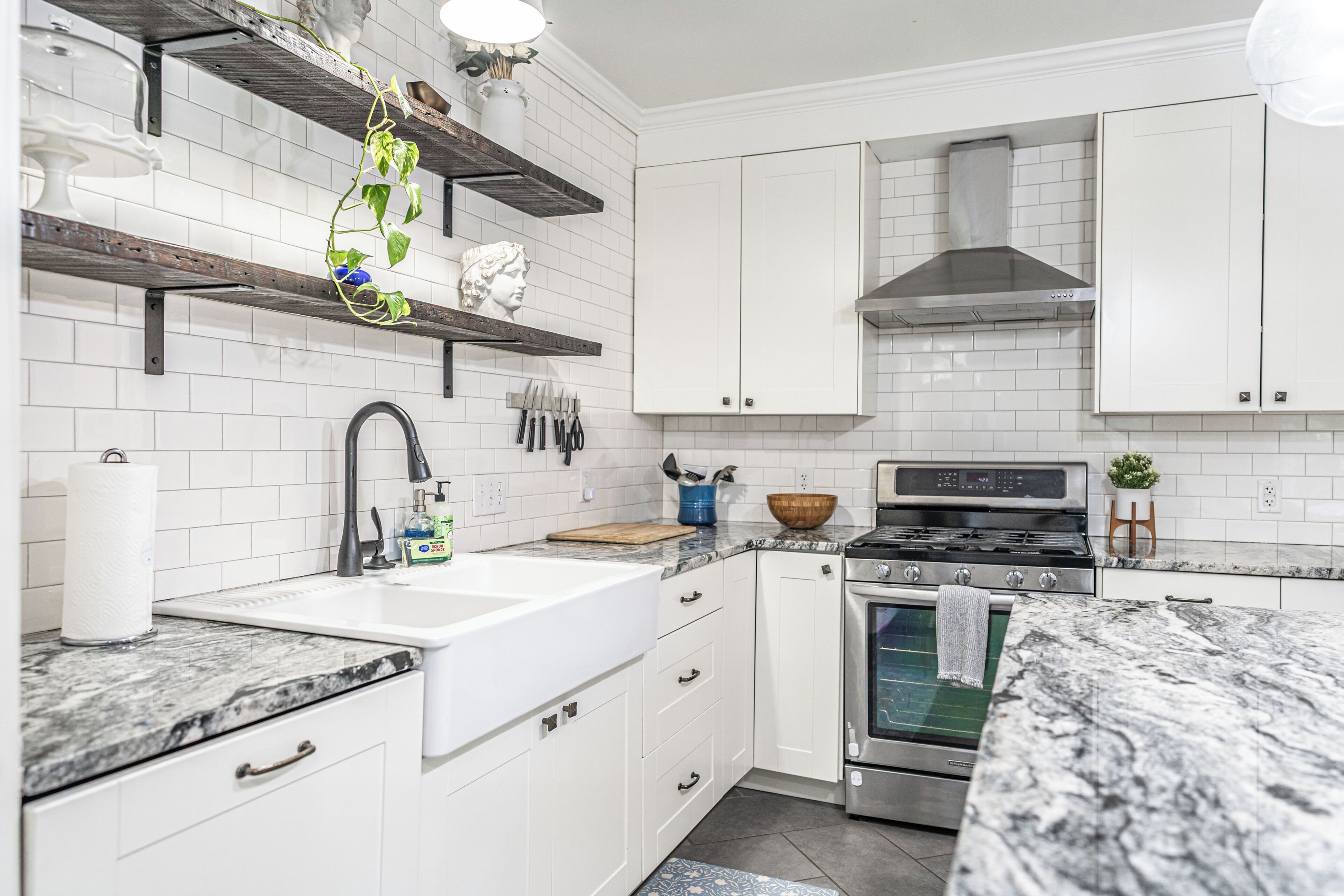 Una cocina moderna con armarios blancos, estufa de acero inoxidable y encimera de mármol.