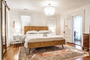 Une chambre à coucher avec un lit, des tables de chevet, un lustre et un tapis à motifs.