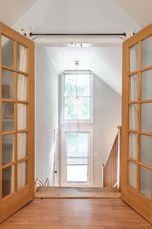 Eine Treppe führt zu einer zweiten Etage mit Holztüren und einem Fenster.