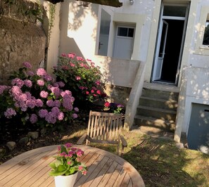 A wooden table with a potted plant, a wooden chair, and a garden with pink flowers. - Charming house in the city center, just a stone's throw from the ocean, with a small garden (Saint-Nazaire)