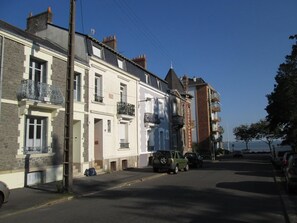 A street with multi-story buildings, a parked car, and a clear sky. - Charming house in the city center, just a stone's throw from the ocean, with a small garden (Saint-Nazaire)