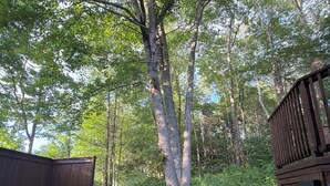 A wooden deck with a bench and a picnic table surrounded by trees.