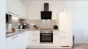 A modern kitchen with white cabinetry, a built-in oven, a coffee maker, and a microwave. - Apartment mit Dachterrasse (Lübeck)