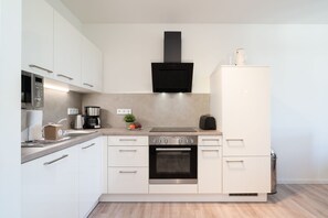 A modern kitchen with white cabinetry, a built-in oven, a coffee maker, and a microwave. - Apartment mit Dachterrasse (Lübeck)