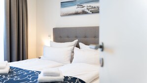 A neatly made bed with white linens and a blue blanket with cursive writing, a grey upholstered headboard, and a painting of a beach scene above the bed. - Apartment mit Dachterrasse (Lübeck)