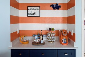 A kitchen counter with a framed newspaper, a coffee machine, a mug, and a mug holder. - A polished oceanfront escape where subtle JAWS-inspired details, thoughtful luxury, and dog-friendly comforts create an unforgettable beach getaway. (Myrtle Beach)