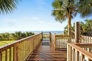A wooden boardwalk leading to a beach with palm trees and a clear sky. - A polished oceanfront escape where subtle JAWS-inspired details, thoughtful luxury, and dog-friendly comforts create an unforgettable beach getaway. (Myrtle Beach)