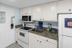 A compact kitchen with white cabinets, a microwave, stove, sink, and a refrigerator. - A polished oceanfront escape where subtle JAWS-inspired details, thoughtful luxury, and dog-friendly comforts create an unforgettable beach getaway. (Myrtle Beach)