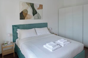 A neatly made bed with white linens and towels, a teal headboard, and a wall-mounted abstract art piece. - Parthenope | Bright 1BR nest in a residential area (Milan)