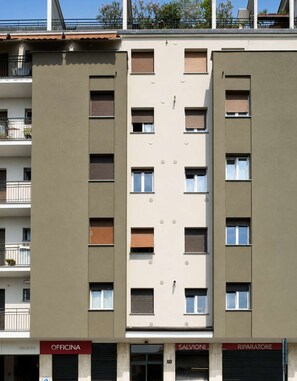 A multi-story building with balconies, a ground-level office, and a visible storefront. - Parthenope | Bright 1BR nest in a residential area (Milan)