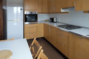 A kitchen with wooden cabinets, a white countertop, a stove, an oven, and a refrigerator. - Parthenope | Bright 1BR nest in a residential area (Milan)