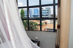 Une pièce avec une grande fenêtre, un lit recouvert de draps blancs et une petite table sur laquelle se trouvent un téléphone et un livre.