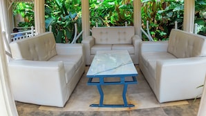 A covered outdoor seating area with white cushioned chairs and a table.