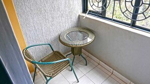 Un balcón en esquina con una silla de mimbre y una mesa de vidrio.