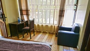 Una habitación de hotel con cama, escritorio, sillón, sofá y ventana con cortinas.