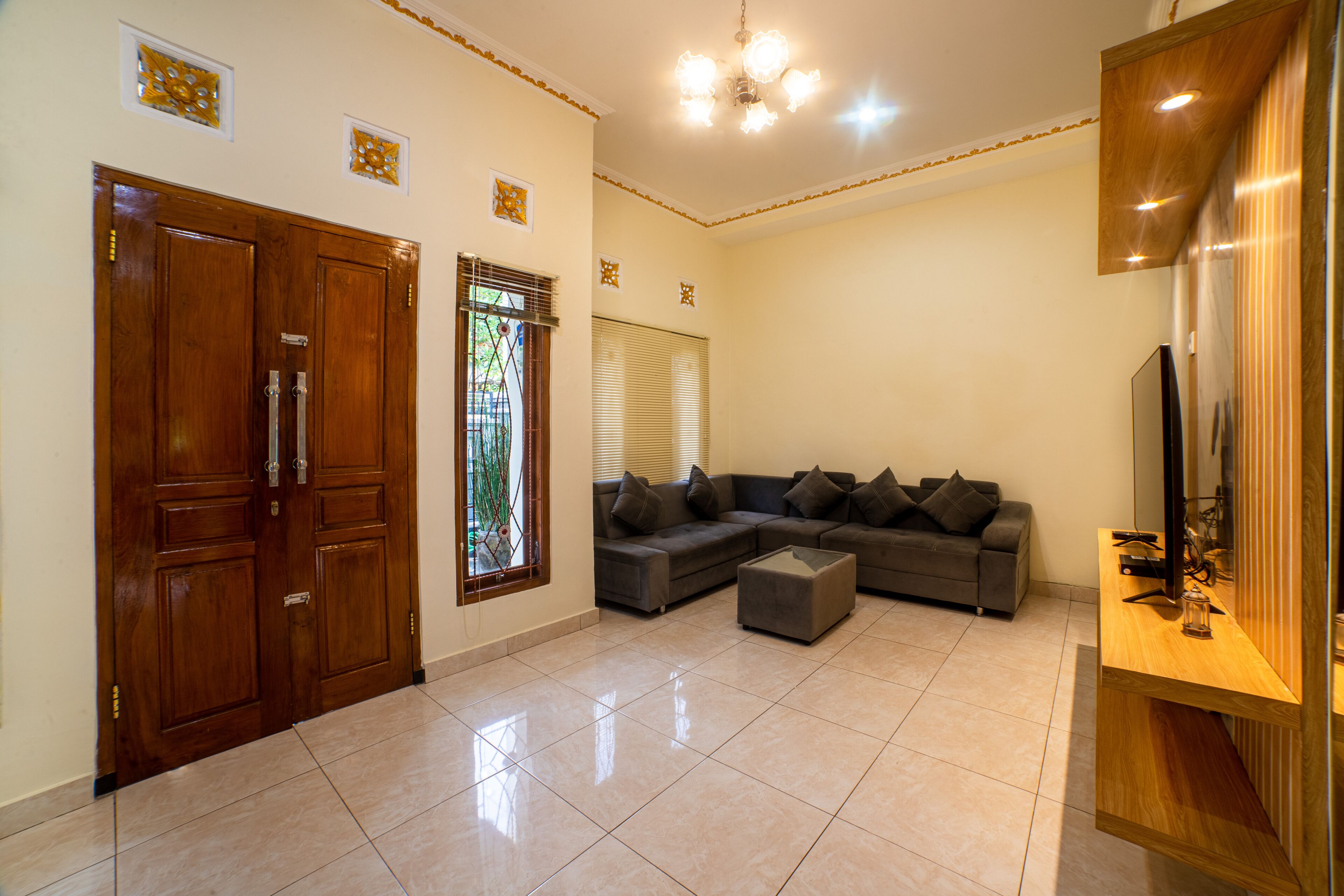 Un salón espacioso con una puerta de madera grande, un sofá seccional, una mesa de centro de vidrio y un televisor sobre un mueble de madera.
