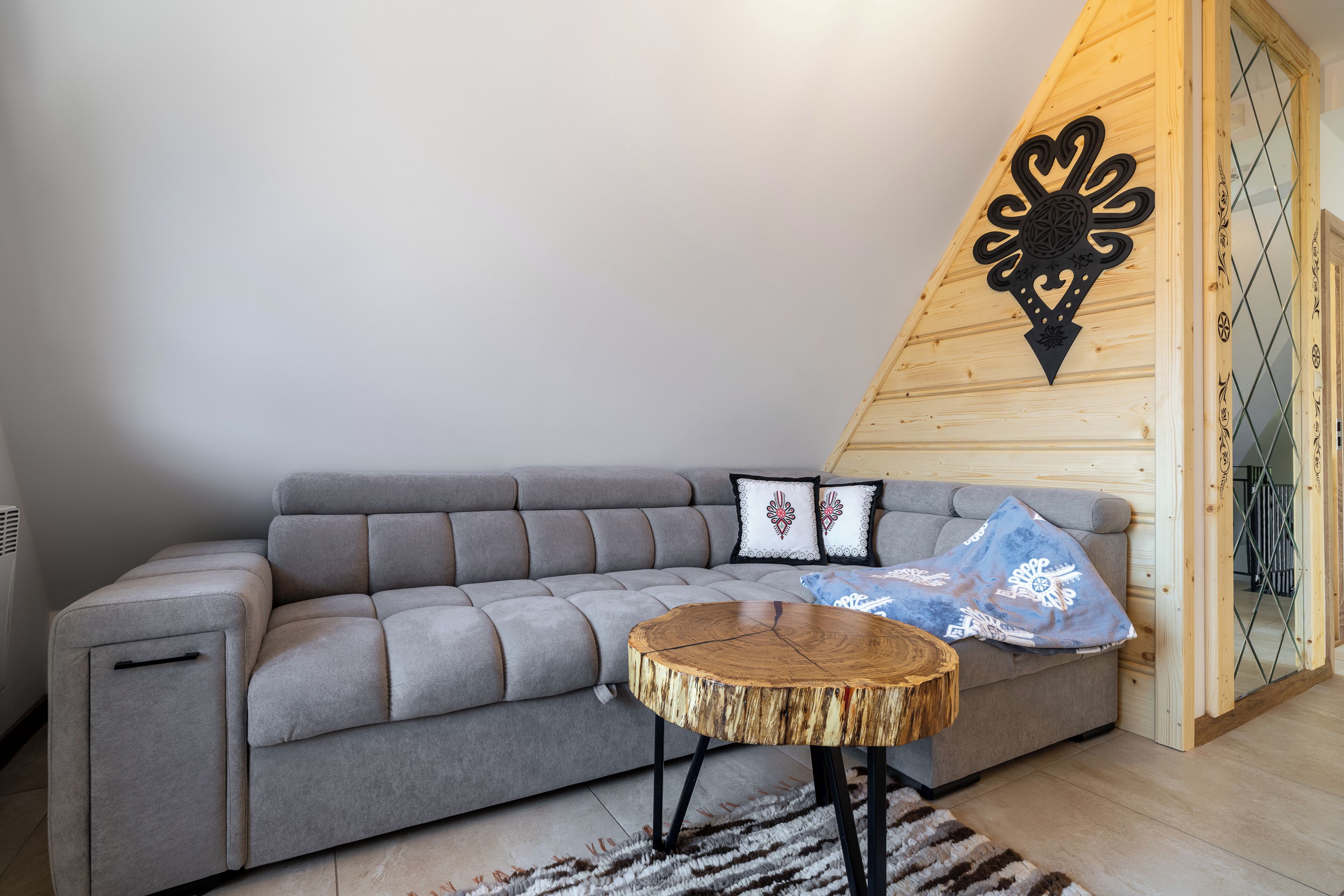 Un salon moderne avec un canapé d’angle gris, une table basse ronde en bois et des coussins décoratifs.