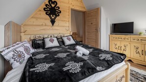 A bedroom with a sloped ceiling, a bed with patterned bedding, a television on a wooden cabinet, and a door leading to another room. - RentPlanet - Apartament Kierpcówka (Kościelisko)