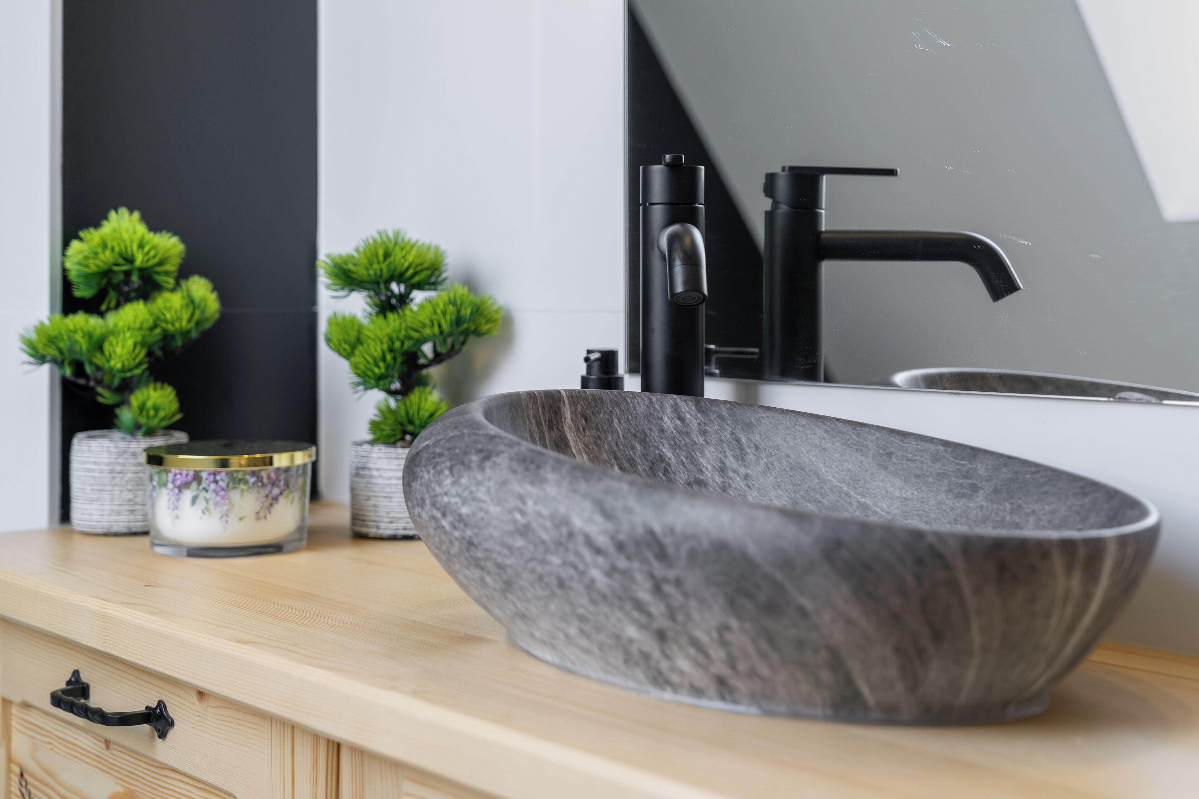 A modern bathroom with a large, oval-shaped vessel sink, a black faucet, and two small potted plants on the counter.
