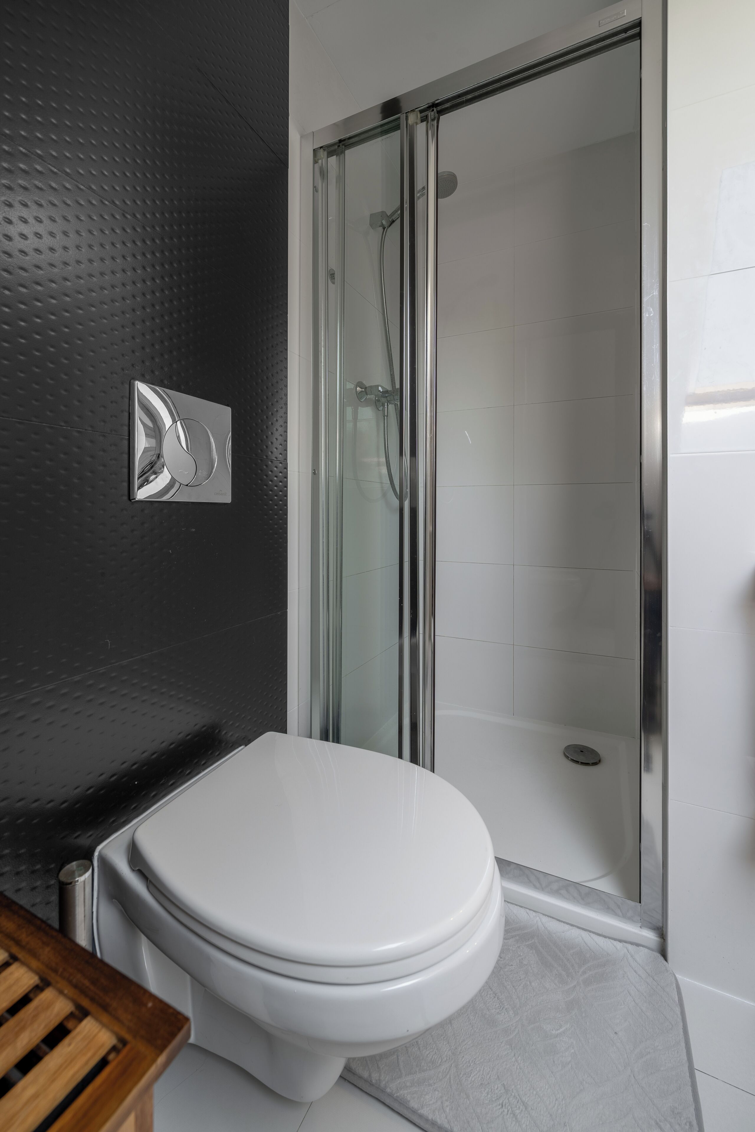 Un baño moderno con inodoro blanco, cabina de ducha de vidrio y pared texturizada en color negro.