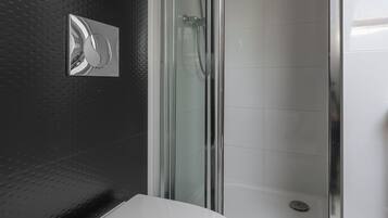 Un baño moderno con inodoro blanco, cabina de ducha de vidrio y pared texturizada en color negro.