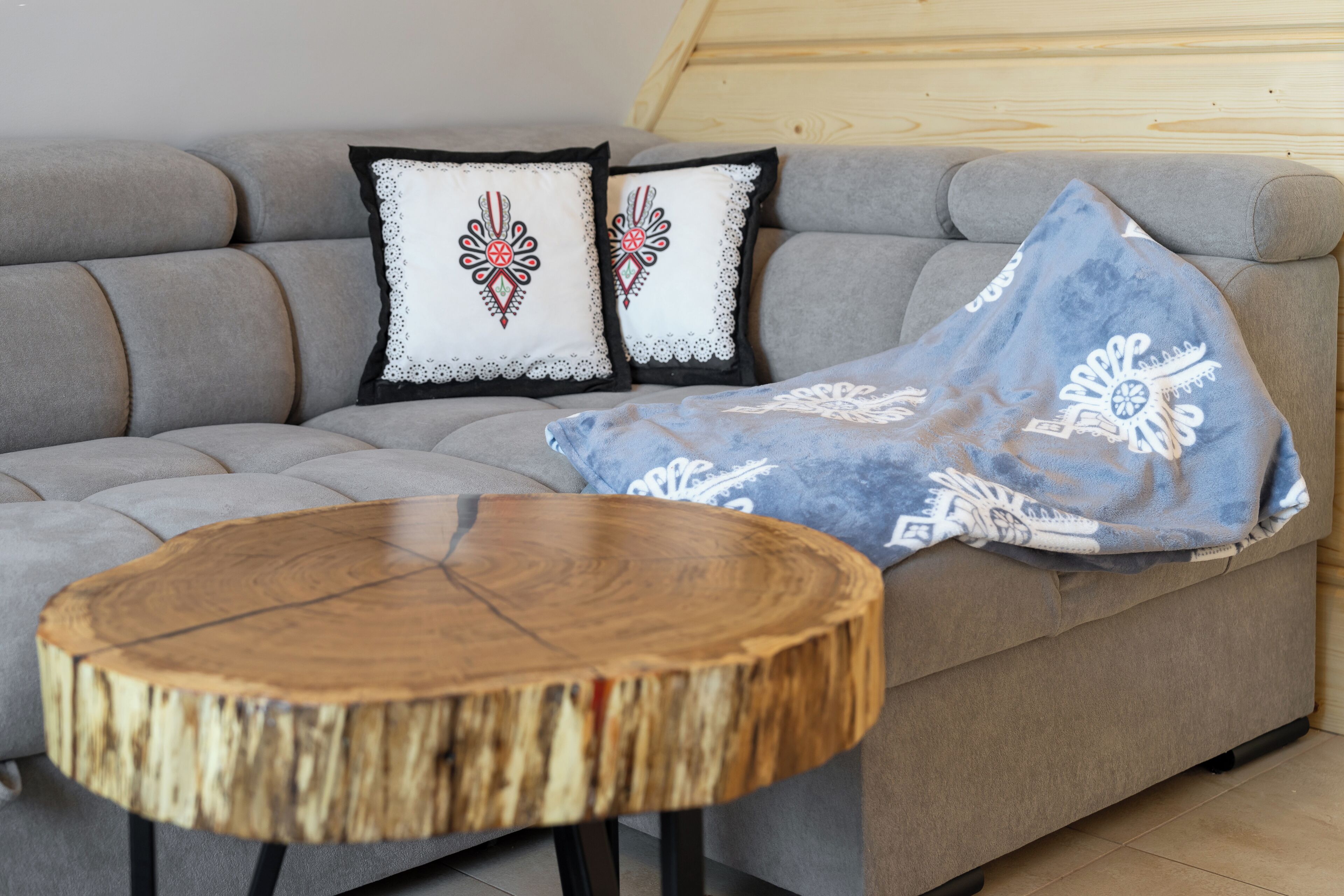 A grey sofa with two decorative pillows, a blue throw blanket, and a round wooden table.