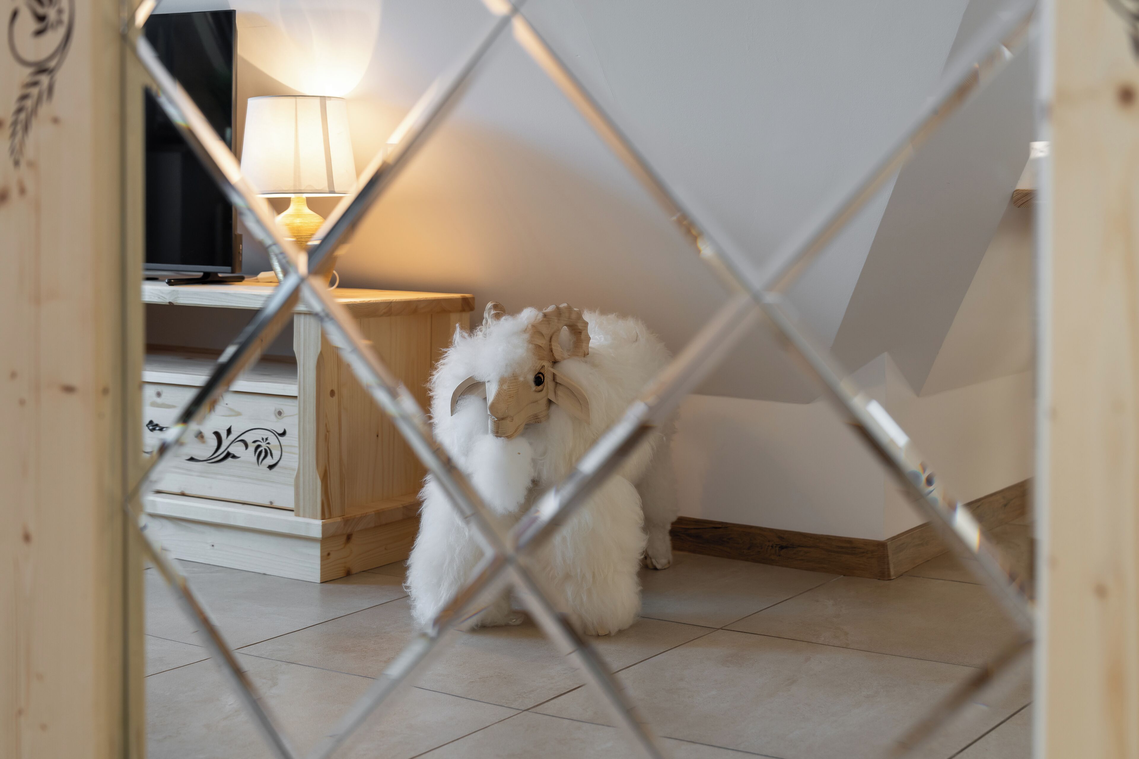 A small, fluffy dog inside a room with a wooden floor, a white wall, and a wooden cabinet with drawers.