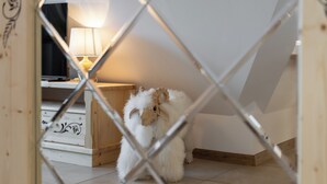 A small, fluffy dog inside a room with a wooden floor, a white wall, and a wooden cabinet with drawers. - RentPlanet - Apartament Kierpcówka (Kościelisko)