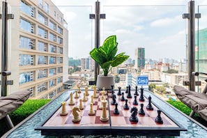A chessboard on a table with a potted plant in the center, overlooking a cityscape. - The Westlands Haven, 2BR,  2 King Beds, Walk to Sarit & GTC,  Gym + Balcony (Nairobi)