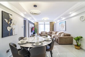 A modern living room with a sofa, a dining table set for four, and a large painting on the wall. - The Westlands Haven, 2BR,  2 King Beds, Walk to Sarit & GTC,  Gym + Balcony (Nairobi)