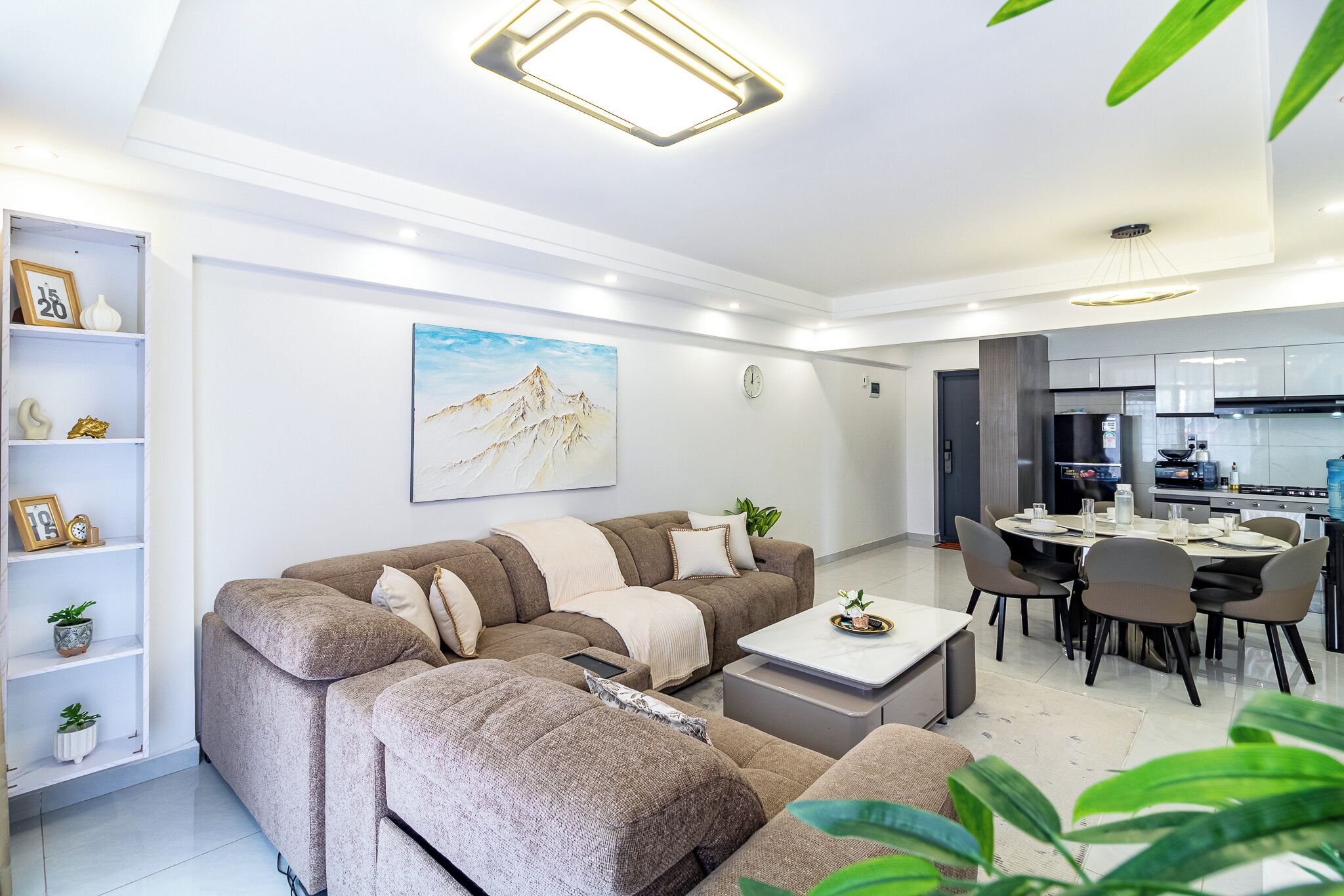 Un salon moderne avec un canapé d’angle, un coin repas avec une table et des chaises, et une cuisine en arrière-plan.