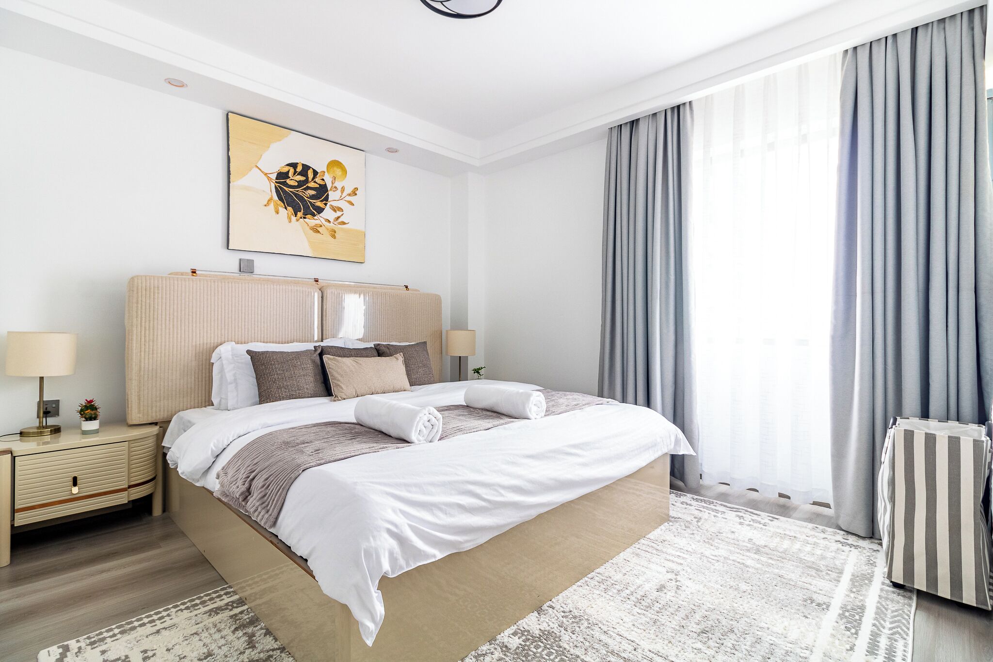 A modern hotel room with a large bed, bedside lamps, a radiator, and a view of the outdoors through curtains.