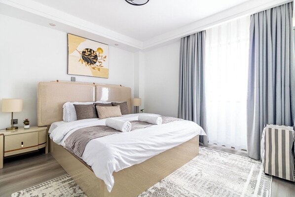 Ein modernes Hotelzimmer mit einem großen Bett, Nachttischlampen, einer Heizung und Blick ins Freie durch Vorhänge.