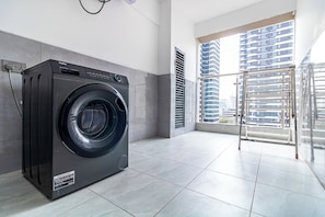 A modern laundry room with a front-loading washer and dryer, large windows, and a view of high-rise buildings. - The Westlands Haven, 2BR,  2 King Beds, Walk to Sarit & GTC,  Gym + Balcony (Nairobi)