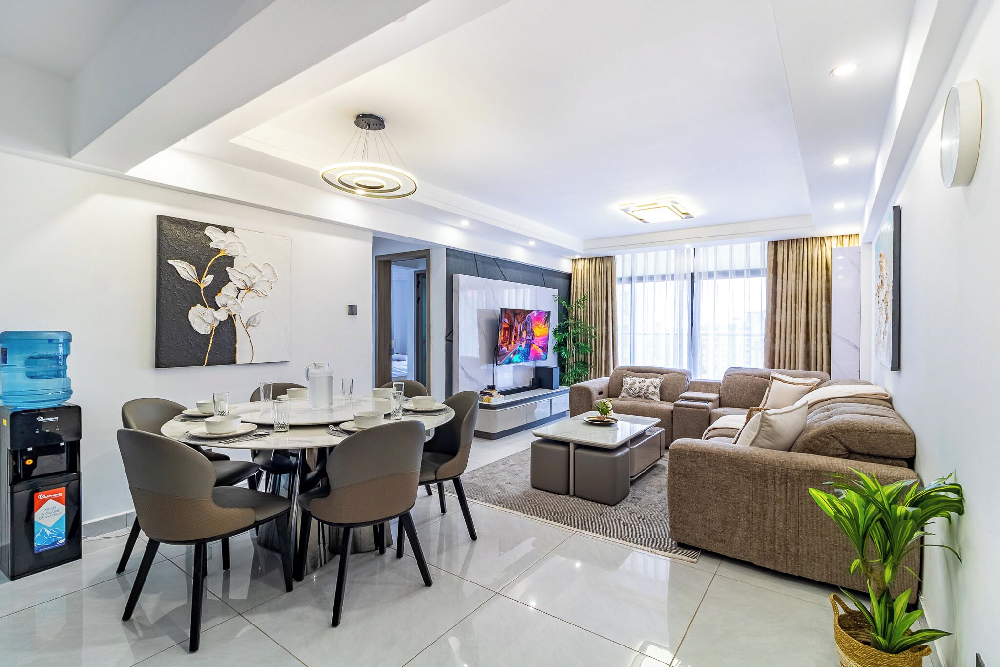 A modern living room with a dining area, a flat-screen TV, and a water dispenser.