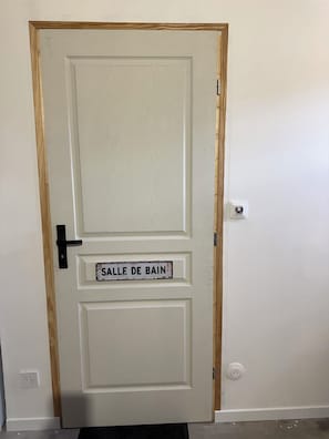Eine weiße Tür mit einem Metallgriff und einem Schild, auf dem 'SALLE DE BAIN' steht, das auf ein Badezimmer hinweist.
