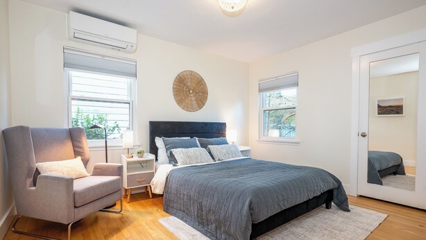 Une chambre à coucher avec un lit, une chaise, une table de chevet, une lampe et une fenêtre.