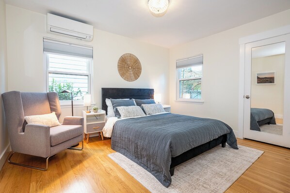 A bedroom with a bed, a chair, a nightstand, a lamp, and a window.