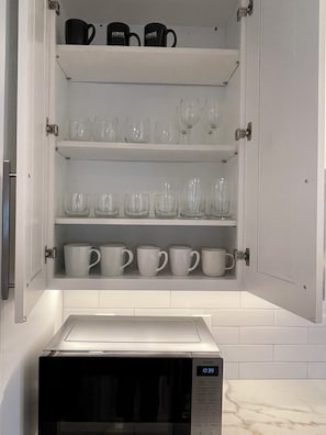 A kitchen cabinet with shelves containing various glassware and mugs.