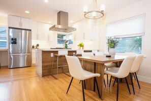 A modern kitchen with a stainless steel refrigerator, wooden cabinets, a central island with seating, and a large window providing natural light. - Cottage with Sauna, Fenced Backyard, Near Stadiums (Seattle)